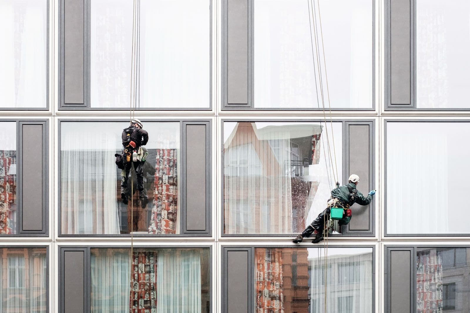 Two window cleaners on ropes washing the glass of a building
