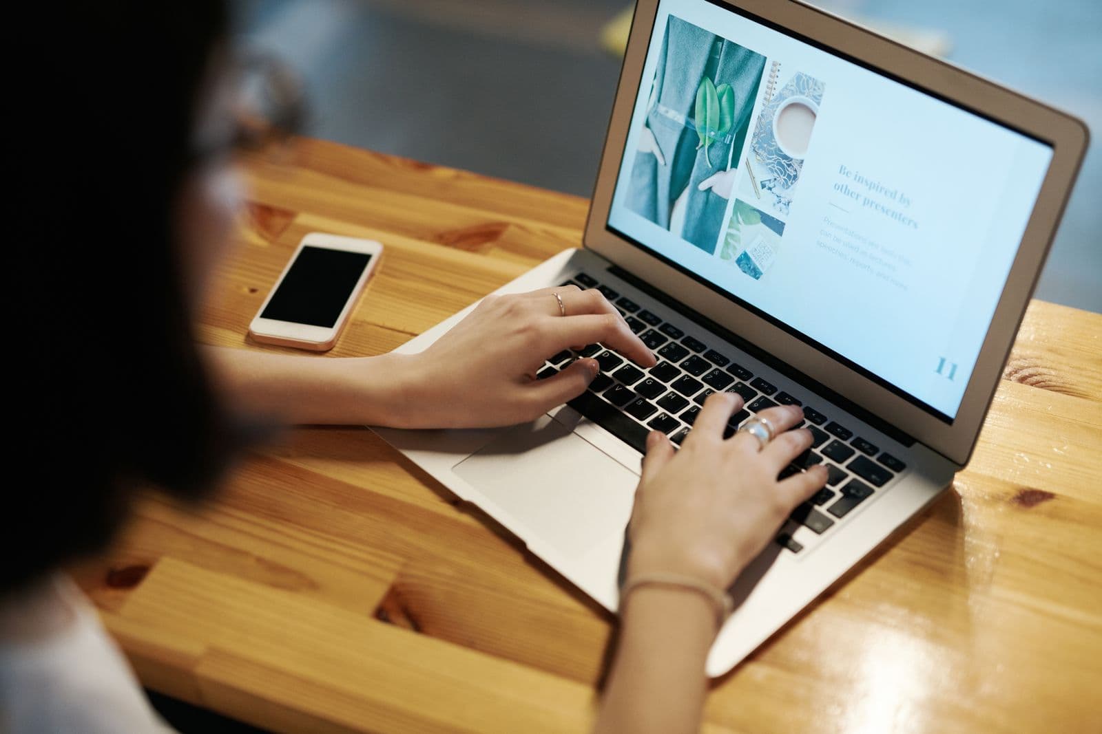 A freelancer's hands typing on a laptop at a wooden desk, phone beside it