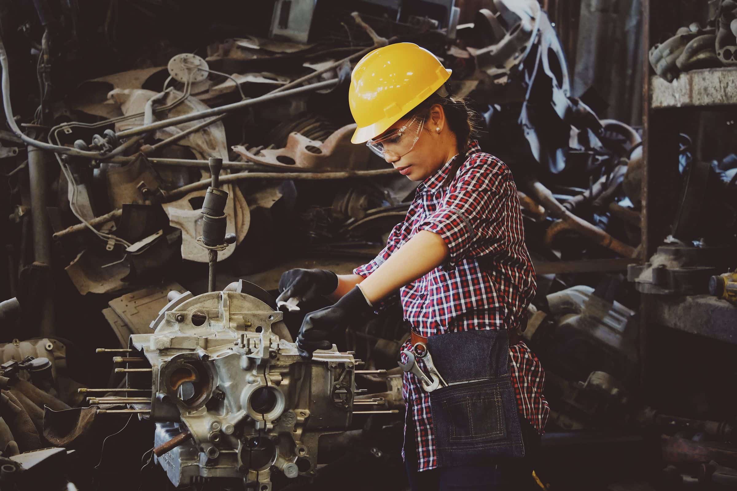 A tradeswoman in a hard hat and safety glasses working on an engine block